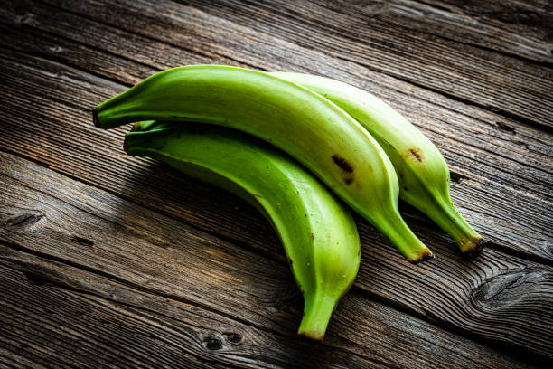 Three green plantains on wooden table Three green plantains on wooden table